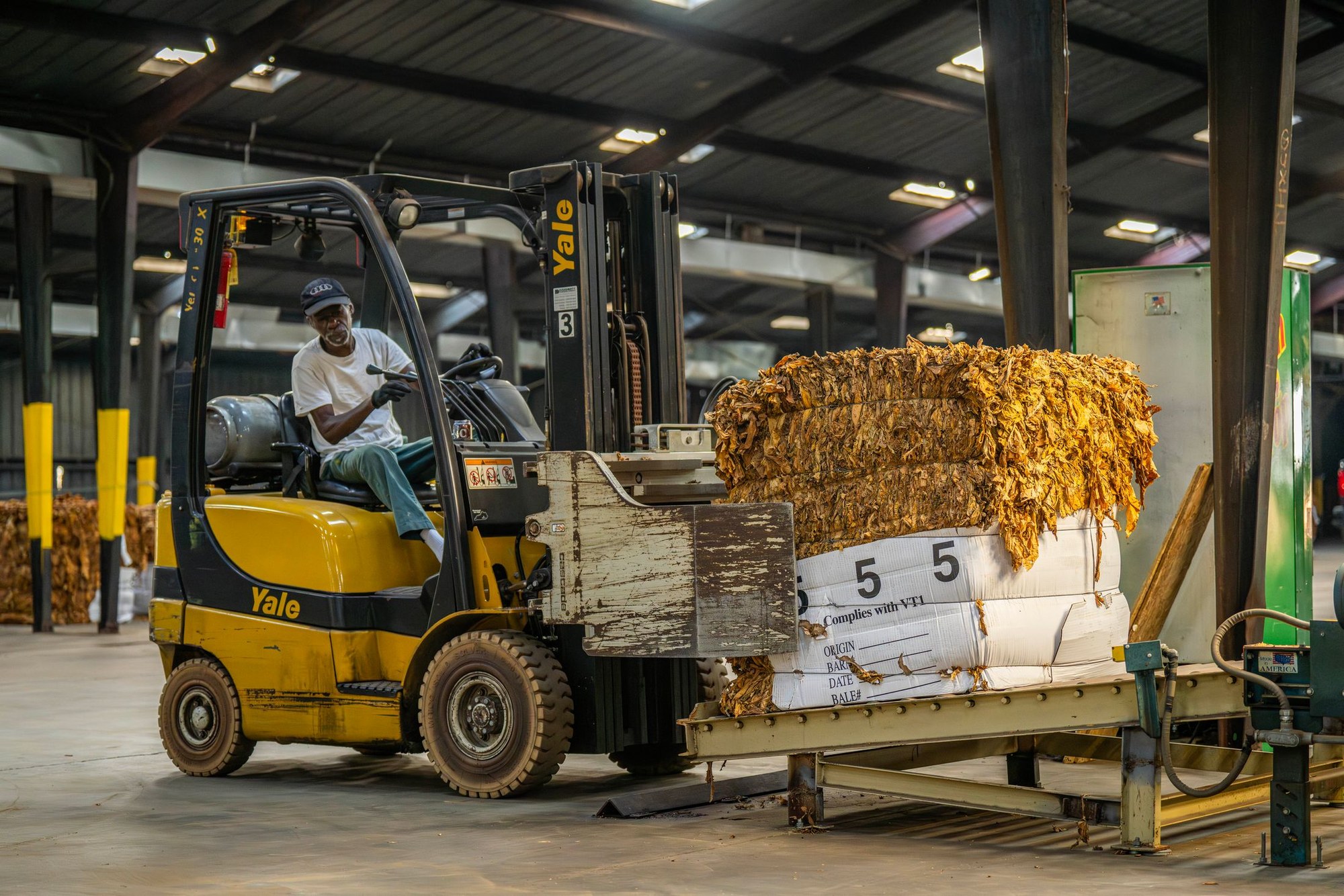 Forklift operator moving a large compressed bale beside industrial handling equipment