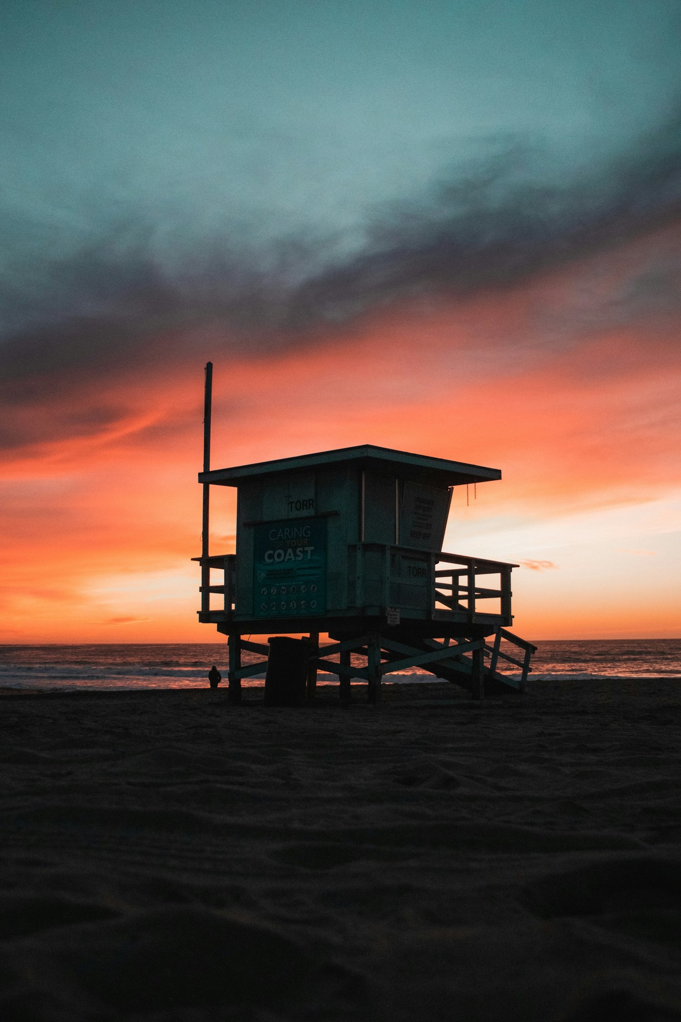 Lifeguard tower silhouetted against an orange sunset above the ocean