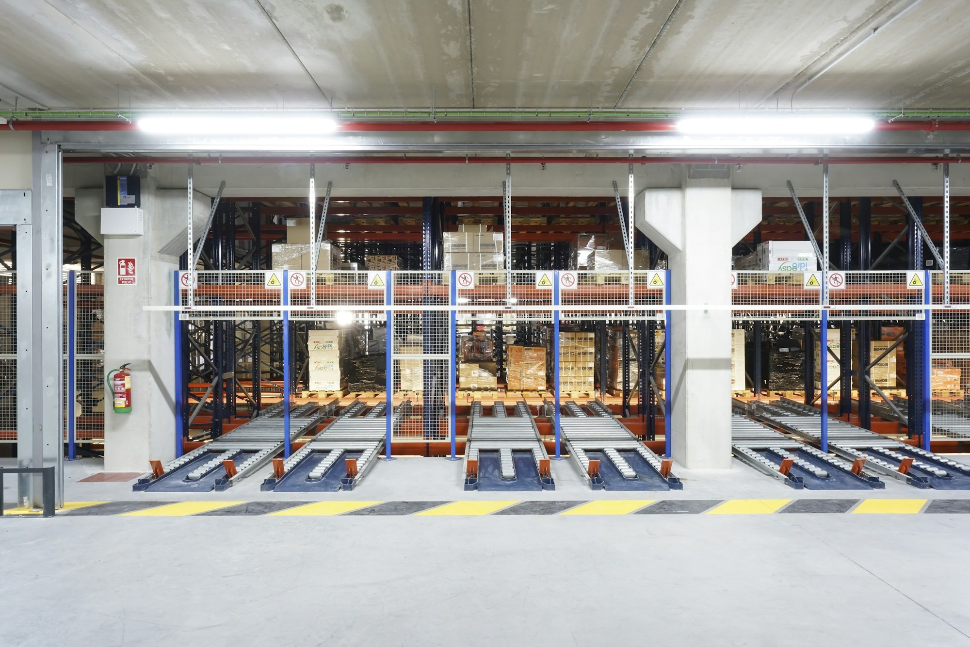 Palletized boxes behind safety fencing and roller conveyors in a warehouse